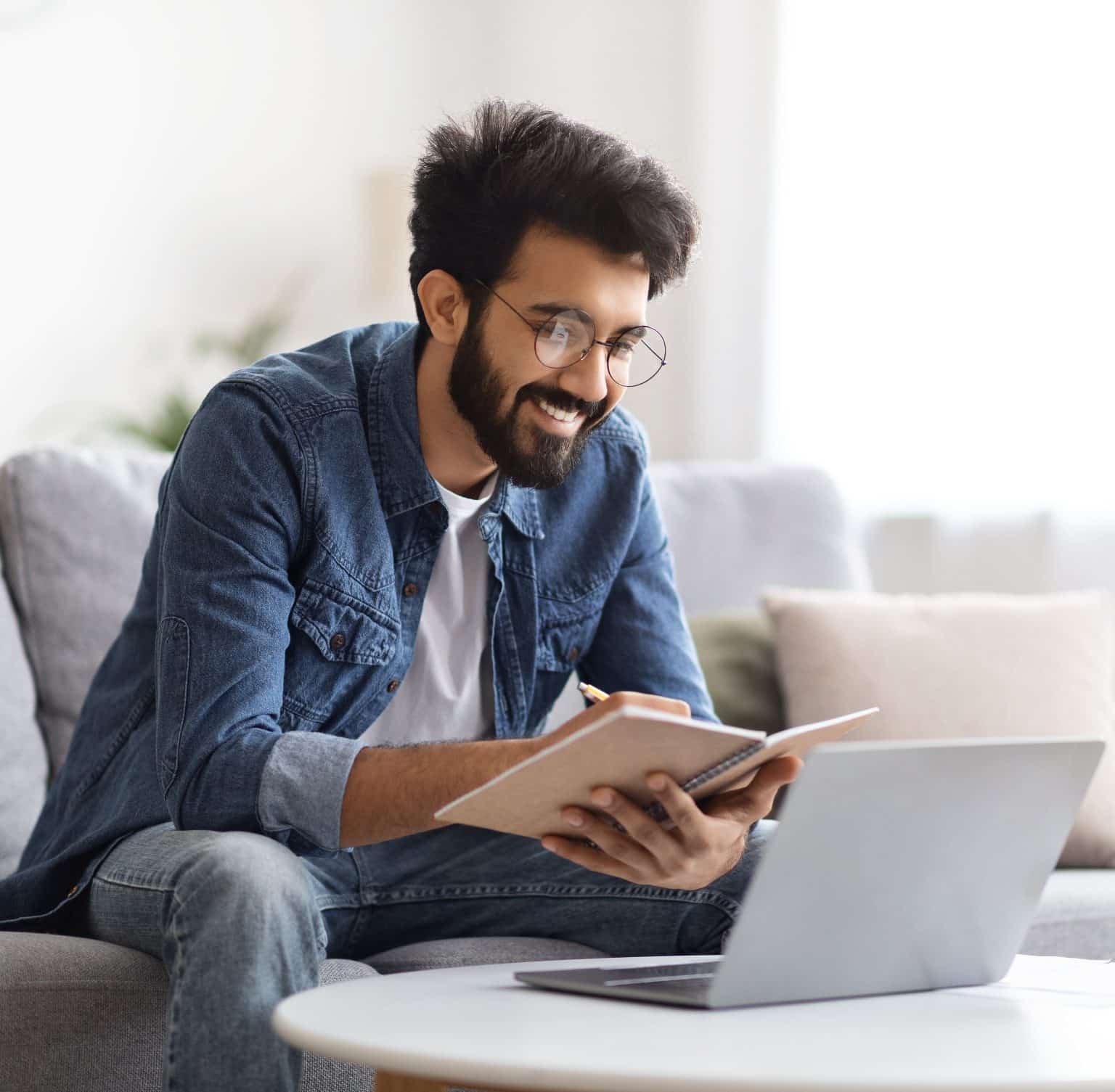 Homme étudiant à distance depuis son domicile, prenant des notes tout en travaillant sur son ordinateur portable